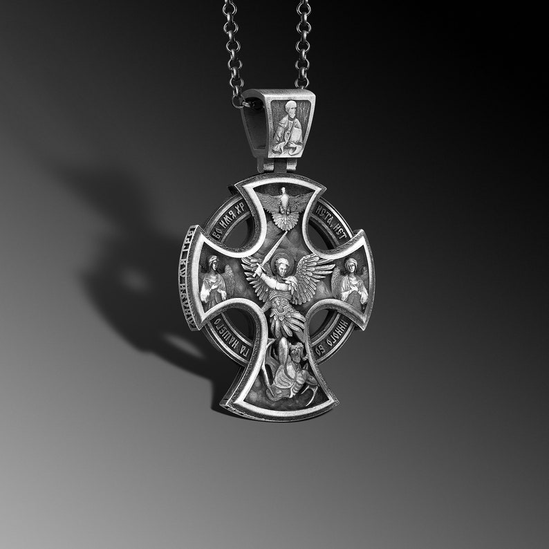 May include: Silver pendant featuring a cross with an angel holding a sword, surrounded by four smaller figures and text in Cyrillic script. The pendant is attached to a silver chain.