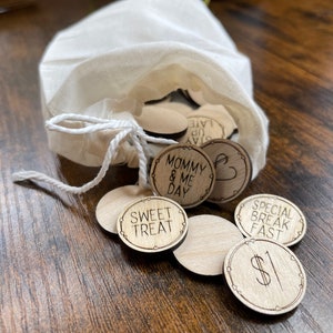 May include: A white muslin bag filled with wooden tokens, each with a different phrase written on it. The phrases include "Mommy & Me Day", "Sweet Treat", "Special Break Fast", and "$1".