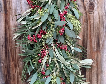 May include: A long garland of green eucalyptus leaves and red berries, hanging against a wooden background.