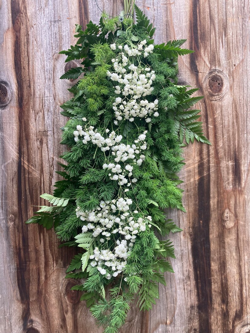 以下が含まれることがあります： 木製の壁に白いカスミソウの花と緑のシダの長いガーランドがぶら下がっている