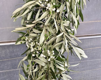 Può includere: Una ghirlanda di rami di olivo e fiori bianchi di gipsofila. La ghirlanda è appesa verticalmente ed è fatta di verde fresco.