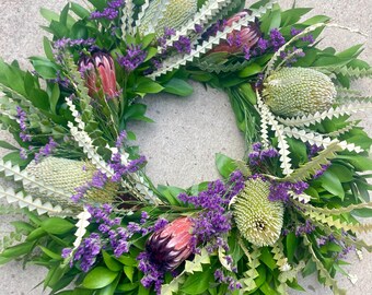 May include: A green wreath with purple flowers and dried brown and beige flowers. The wreath is made of leaves and branches.