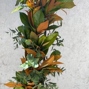 May include: A garland of green and brown leaves, likely magnolia and eucalyptus, arranged in a vertical line.