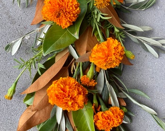 May include: A vibrant floral arrangement featuring bright orange marigold blooms, olive branches, and brown magnolia leaves. The composition showcases a mix of textures and colors, perfect for seasonal decor or crafting projects.