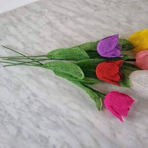May include: A bouquet of six beaded tulips in various colors, including pink, red, white, yellow, and purple. The tulips are made of small beads and have green stems.
