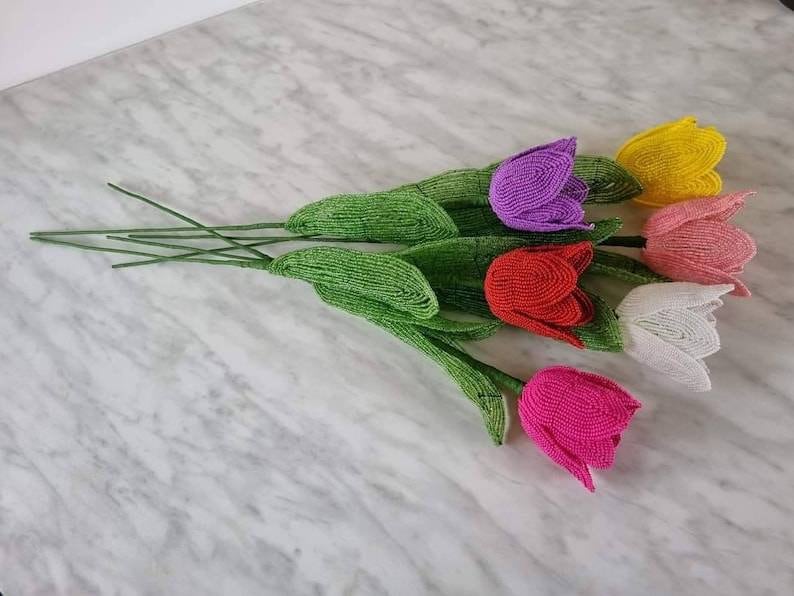 May include: A bouquet of six beaded tulips in various colors, including pink, red, white, yellow, and purple. The tulips are made of small beads and have green stems.