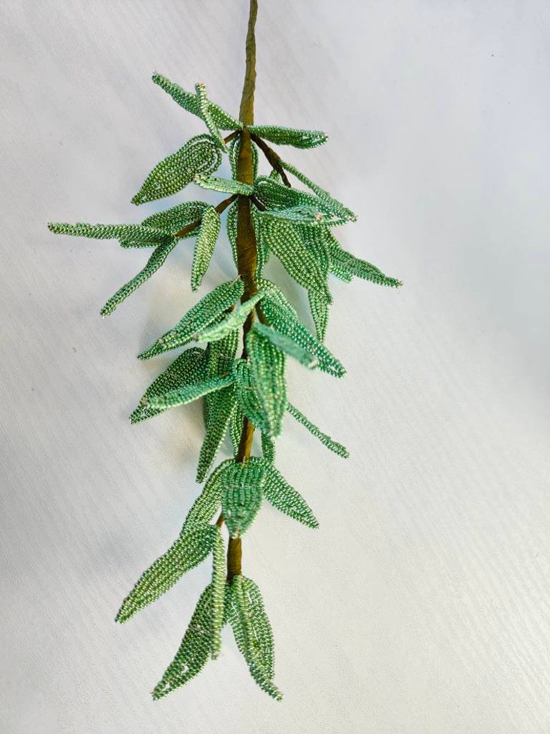 May include: A green beaded garland with leaves, resembling a branch of a plant. The garland is made of small green beads and is strung on a brown wire.