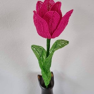 May include: A pink beaded tulip flower with green beaded leaves in a black vase.