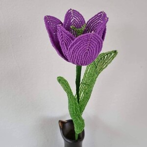 May include: A purple beaded tulip with green beaded leaves in a black vase.
