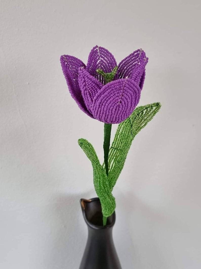 May include: A purple beaded tulip with green beaded leaves in a black vase.