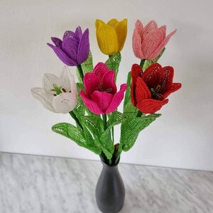 May include: A bouquet of six beaded tulips in a black vase. The tulips are white, yellow, pink, red, purple, and fuchsia.