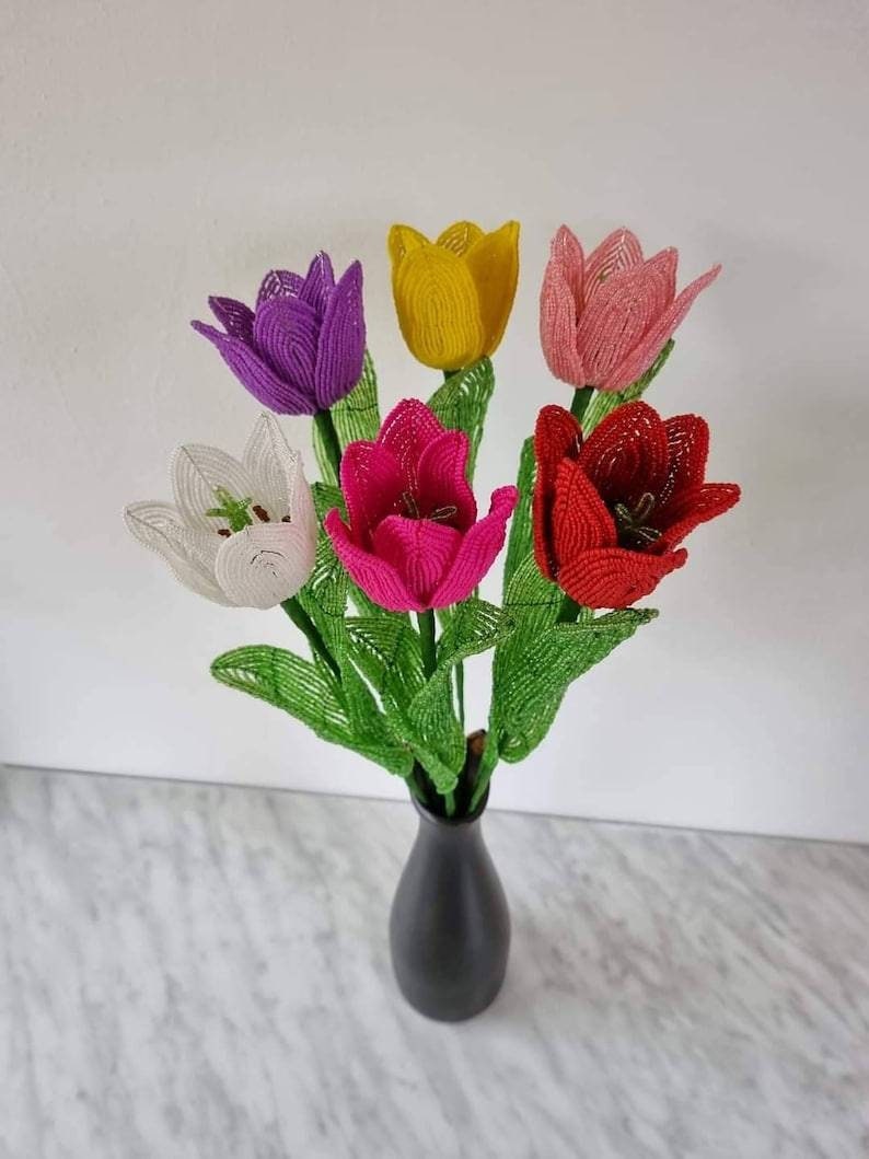 May include: A bouquet of six beaded tulips in a black vase. The tulips are white, yellow, pink, red, purple, and fuchsia.