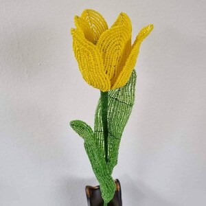 May include: A yellow beaded tulip with green beaded leaves in a black vase.