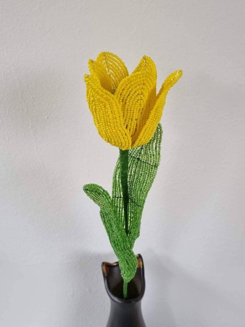May include: A yellow beaded tulip with green beaded leaves in a black vase.