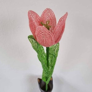 May include: A pink beaded tulip with green beaded leaves in a black vase.