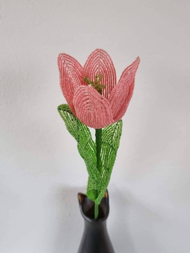 May include: A pink beaded tulip with green beaded leaves in a black vase.