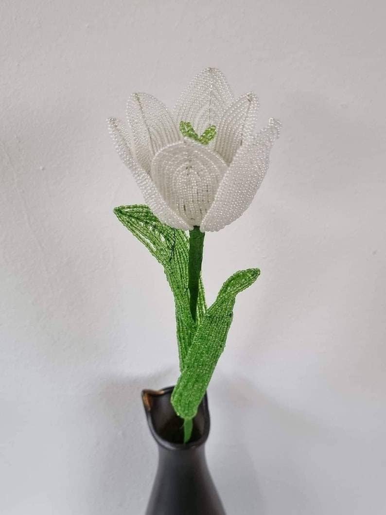 May include: A white beaded tulip with green beaded leaves in a black vase.