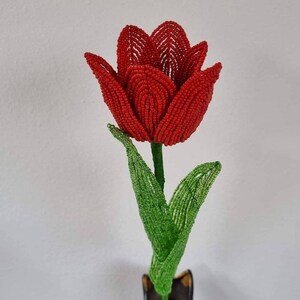 May include: A red beaded tulip flower with green beaded leaves in a black vase.