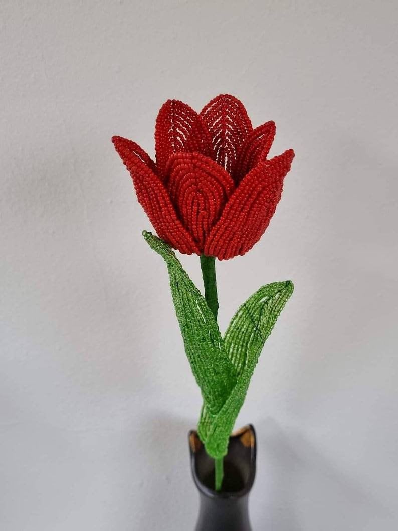 May include: A red beaded tulip flower with green beaded leaves in a black vase.