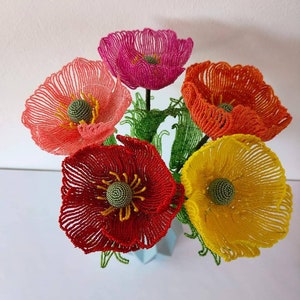 K&ouml;nnte beinhalten: Ein Strau&szlig; aus f&uuml;nf Perlenblumen in einer Vase. Die Blumen sind rot, orange, gelb, rosa und in einem helleren Rosaton. Die Blumen sind aus kleinen Perlen gefertigt und haben ein realistisches Aussehen.