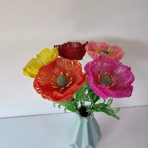 K&ouml;nnte beinhalten: Ein Strau&szlig; aus f&uuml;nf Perlen-Mohnblumen in einer hellblauen Vase. Die Blumen sind rot, orange, gelb, rosa und dunkelrosa. Die Blumen sind aus kleinen Perlen gefertigt und haben ein realistisches Aussehen.
