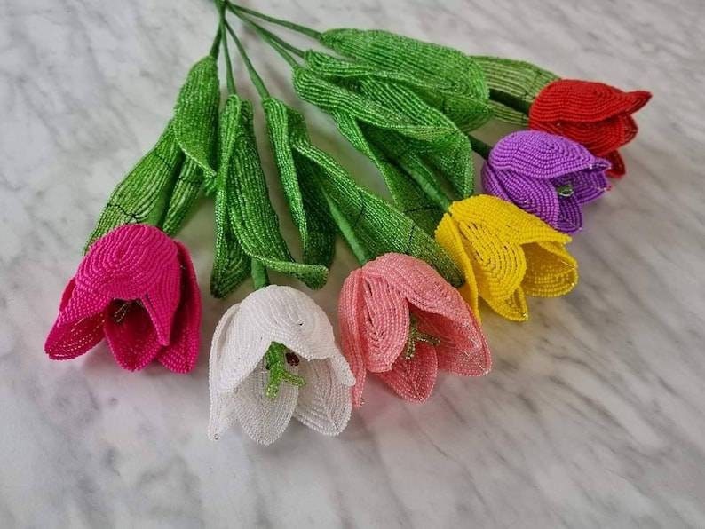 May include: A bouquet of beaded tulips in various colors, including pink, white, yellow, purple, and red. The tulips are handmade and have green beaded stems.