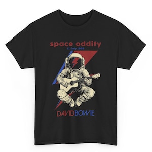 May include: Black t-shirt with a graphic of an astronaut playing a guitar. The astronaut has a lightning bolt design on their helmet. The text "space oddity 11 July 1969" and "DAVID BOWIE" are printed on the shirt.