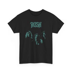 May include: Black t-shirt featuring a teal green graphic of the band Rush. The graphic includes the band's name and three band members' faces.