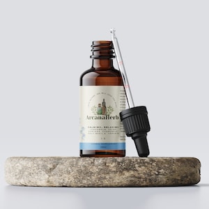 Może przedstawiać: Brązowa szklana butelka z kroplomierzem, oznaczona jako "ArcanaHerb" i "Calming, Relaxing" z listą składnik&oacute;w, w tym melisa, reishi, damiana, rumianek, święty bazylia i werbena. Butelka stoi na okrągłym, jasnobrązowym kamieniu.