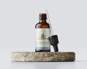 Może przedstawiać: Brązowa szklana butelka z kroplomierzem, oznaczona jako "ArcanaHerb" i "Calming, Relaxing" z listą składników, w tym melisa, reishi, damiana, rumianek, święty bazylia i werbena. Butelka stoi na okrągłym, jasnobrązowym kamieniu.