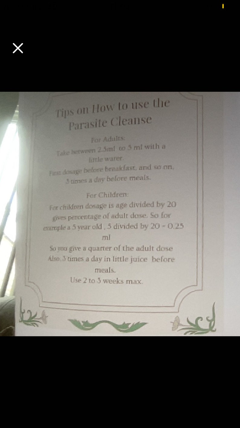 May include: A white sheet of paper with black text outlining instructions on how to use a parasite cleanse. The text includes dosage information for adults and children, as well as the frequency and duration of use. The paper has a decorative border with green floral designs.