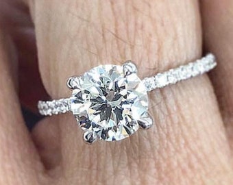 May include: A silver engagement ring with a large round diamond center stone and a band of smaller diamonds.