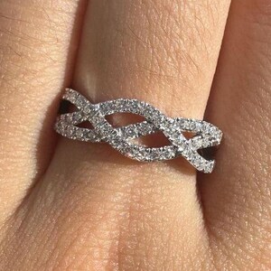 Puede incluir: Un anillo de banda de plata con un diseño trenzado adornado con pequeñas piedras transparentes.
