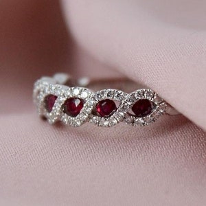 以下が含まれることがあります： 波打つデザインのシルバーのバンドリング。赤い宝石が5つと、小さな透明な宝石が散りばめられています。