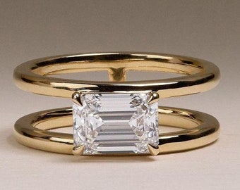 May include: A gold ring with a double band design features a large, clear emerald-cut diamond.