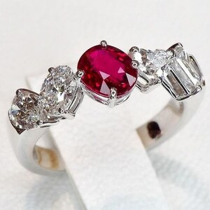 May include: A silver ring with a red ruby gemstone and smaller white diamonds. The ring has a delicate design with the ruby in the center and the diamonds surrounding it.