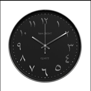 Pu&ograve; includere: Un orologio da parete nero con numeri arabi e lancette argentate. Il quadrante dell'orologio recita "R&M Orient Quartz".