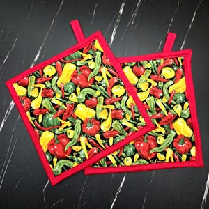 May include: Two square potholders with a vibrant pepper print in red, yellow, and green on a black background. The potholders have a red border and a small red loop for hanging. The design features various types of peppers.