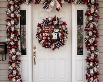 May include: A white front door decorated with a Christmas garland and wreath featuring red, black, and white plaid ribbons, burlap accents, and red ornaments. The wreath includes a sign reading There's Snow place like HOME with a snowman.