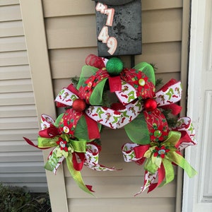 May include: A black mailbox with the numbers 47 and 49 on it, decorated with a green and red Christmas wreath with bows and baubles.