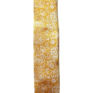 Op de afbeelding: Close-up van een decoratief lint. Het lint heeft een gele achtergrond met een wit bloemmotief. Het getextureerde materiaal is geschikt voor knutselen, cadeauverpakking of andere decoratieve doeleinden.
