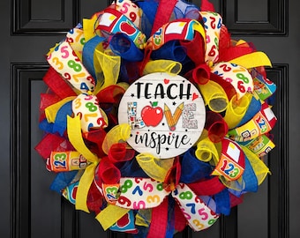 May include: A round decorative wreath featuring red, blue, and yellow mesh ribbons with patterns of numbers, apples, and school supplies. A central white circular sign displays the text TEACH LOVE INSPIRE with a red apple and pencil graphic.