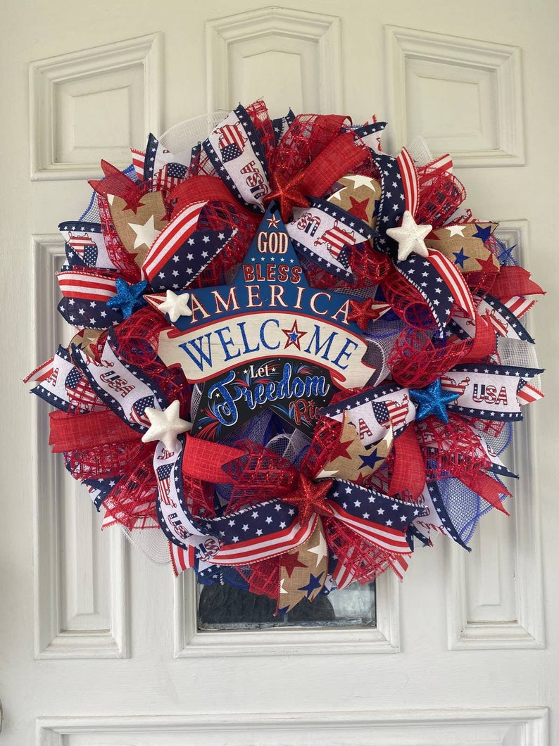 Pu&ograve; includere: Una ghirlanda patriottica rosso, bianco e blu con un cartello che recita "God Bless America Welcome Let Freedom Ring". La ghirlanda &egrave; decorata con stelle, nastri e rete.