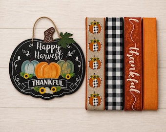 Puede incluir: Un letrero negro con forma de calabaza con el texto Happy Harvest y Thankful, que presenta calabazas y girasoles pintados, acompañado de cuatro rollos de cinta con patrones que incluyen calabazas, cuadros blancos y negros y naranja sólido.