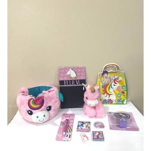 Könnte beinhalten: Ein Geschenkset zum Thema Einhorn mit einem rosa Einhorn-Plüschtier, einer rosa Einhorn-Schale, einem rosa und blauen Einhorn-Notizbuch, einem rosa und blauen Einhorn-Bleistift, einem rosa und blauen Einhorn-Aufkleber, einem rosa und blauen Einhorn-Spiegel und einer rosa und blauen Einhorn-Tasche. Das Notizbuch hat das Wort "Believe" auf dem Cover.