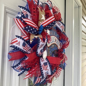 Pu&ograve; includere: Una ghirlanda patriottica rosso, bianco e blu con un cartello che dice "God Bless America Welcome Let Freedom Ring".