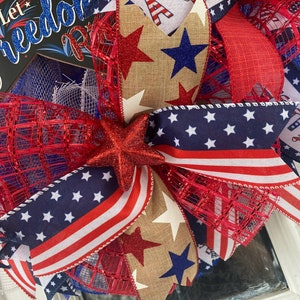 Pu&ograve; includere: Una ghirlanda patriottica rosso, bianco e blu con un fiocco di juta, stelle e un cartello che dice "Let Freedom Ring".