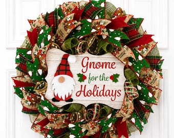 Puede incluir: Una corona navideña decorativa con capas de cintas de malla verdes, rojas y bronceadas con patrones de cuadros. Un letrero central de madera con textura de veta muestra una ilustración de un gnomo y el texto Gnome for the Holidays en rojo.