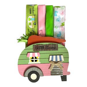 May include: A green and pink wooden camper with a sign that reads "Easter Blessings". The camper is decorated with a carrot, green and pink ribbon, and a bow.