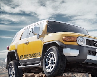 May include: A yellow Toyota FJ Cruiser off-road vehicle driving on a rocky terrain. The vehicle has black accents and the words "FJ Cruiser" and "Toyota" are visible on the front.
